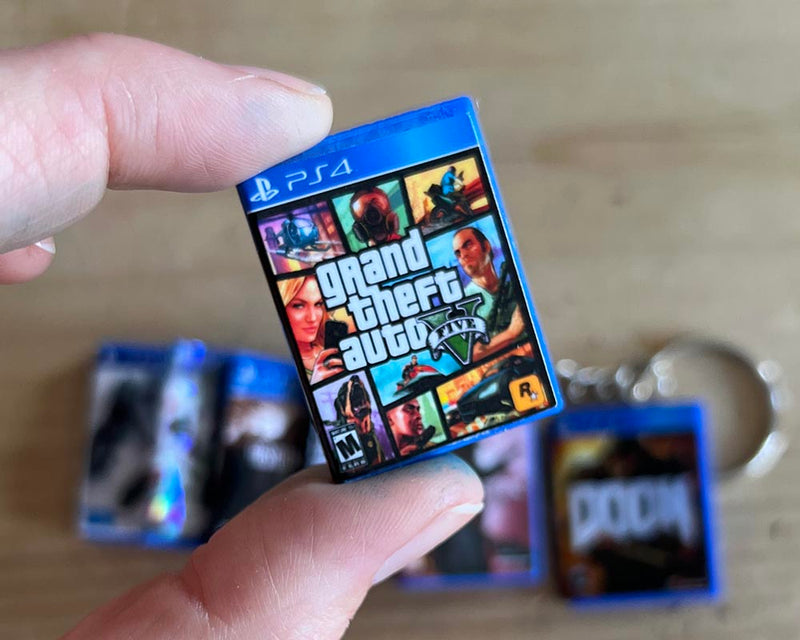 Mini PS4 game case keychain featuring GTA V held between fingers —  retro gamer gift by Loonar 3D